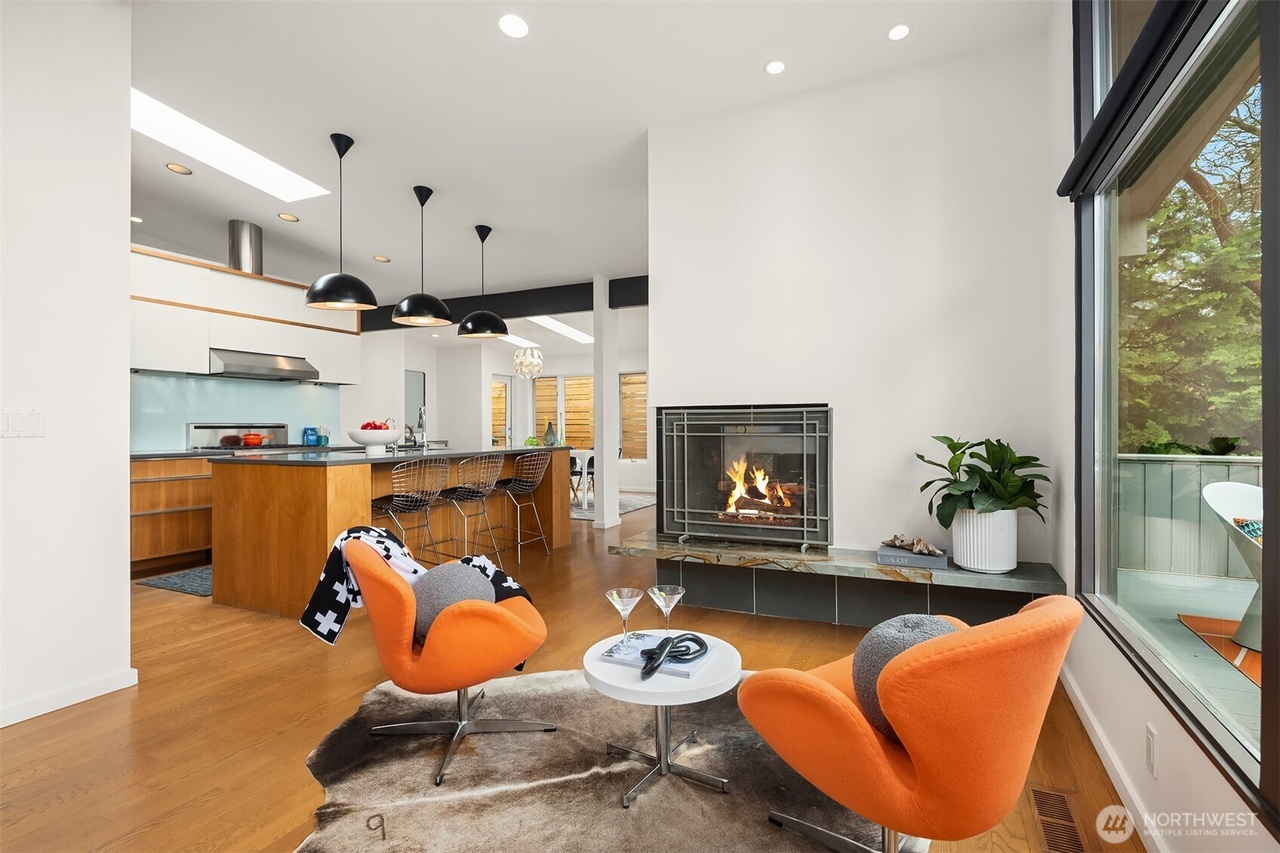 Open-concept modern living space with orange swivel chairs and lit fireplace