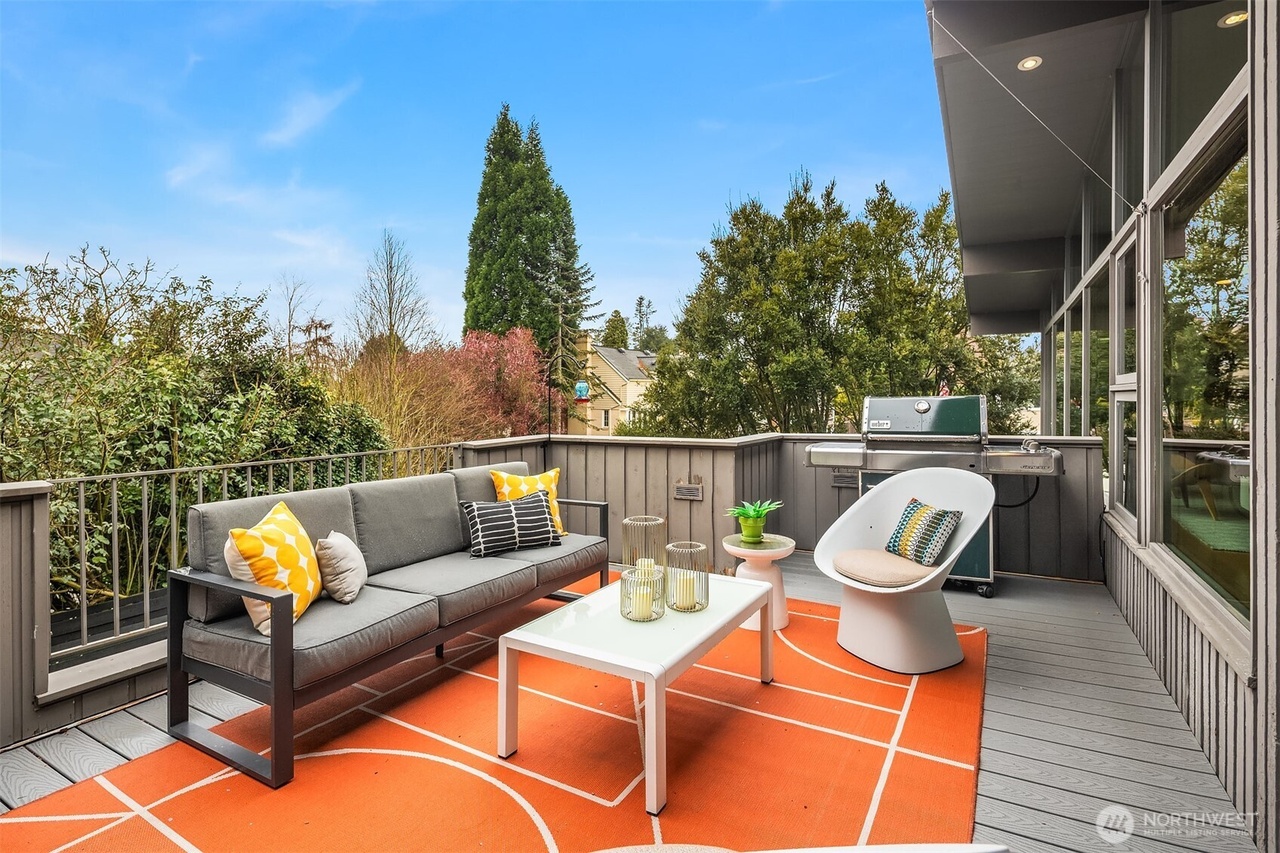 Covered outdoor deck lounge with tailored grey sofa and geometric orange rug