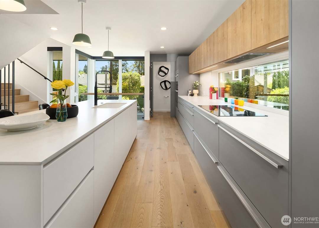 Contemporary kitchen with long white island and sleek grey and wood cabinetry