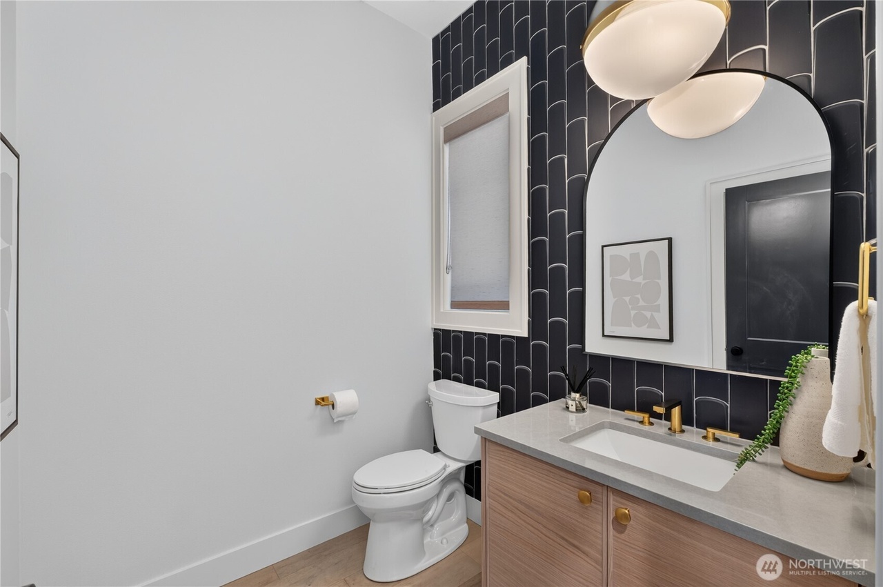 Powder room with curved black tile accent wall and light wood vanity