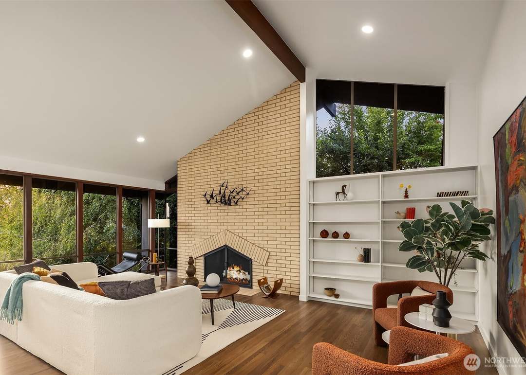 Mid-century modern living room with brick fireplace, vaulted wood beam ceiling, and leafy window views