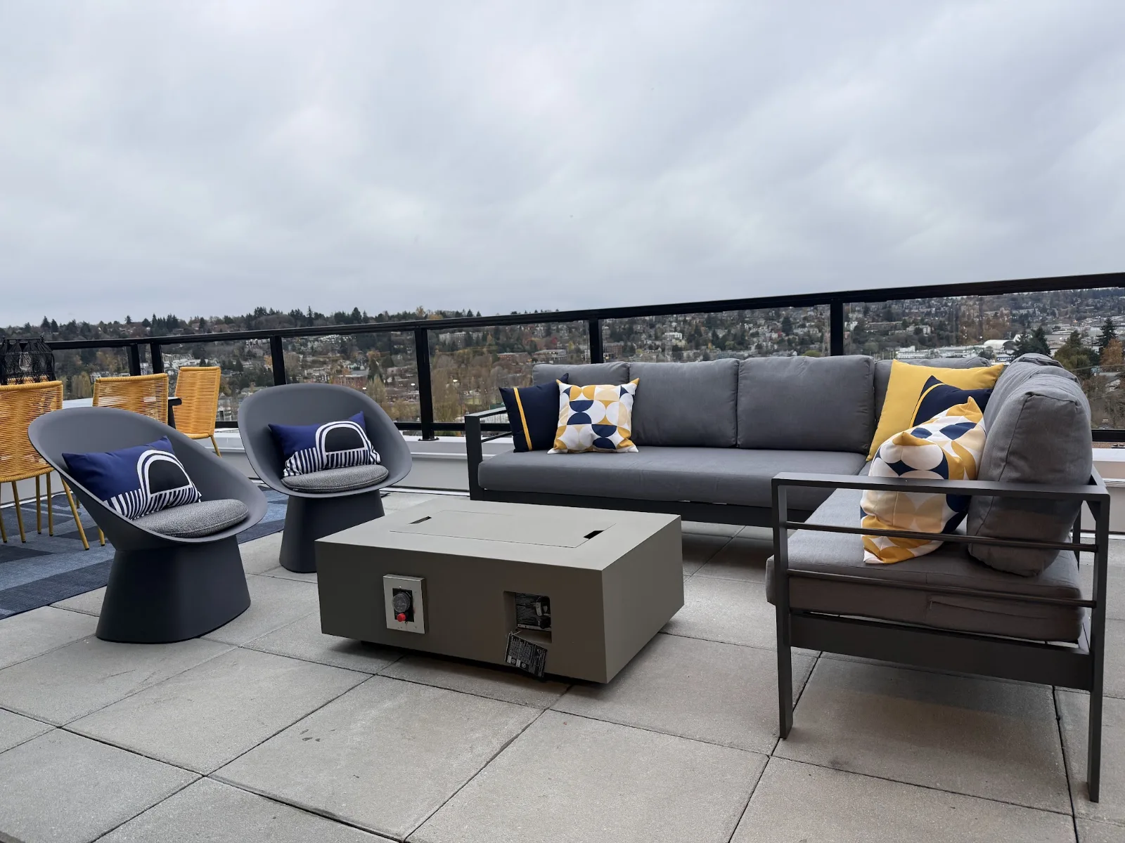 Shared resident rooftop lounge featuring a modular sectional, dark accent chairs, and fire table overlooking Seattle