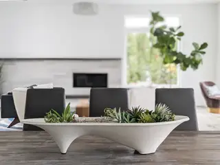 A white sculptural planter filled with succulents sits as a centerpiece on a dark wooden dining table