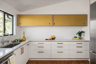 Blue Ridge Remodel: A mid-century modern kitchen features mustard yellow upper cabinets, sleek white lower cabinetry, and terrazzo countertops against a white tiled backsplash