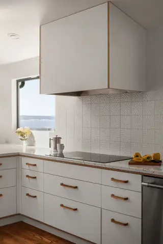 Blue Ridge Remodel: A modern white kitchen features sleek cabinetry with wooden handles, an induction cooktop, and a textured geometric tile backsplash beneath a boxy range hood