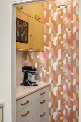 Blue Ridge Remodel: Mustard yellow upper cabinetry and retro geometric wallpaper anchor a stylish kitchen pantry nook featuring a terrazzo countertop and black stand mixer