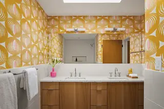Blue Ridge Remodel: A mid-century modern bathroom features bold yellow patterned wallpaper, a dual-sink wooden vanity with terrazzo countertops, and a large mirror