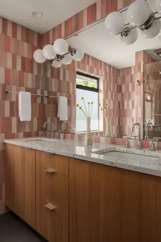 Blue Ridge Remodel: A modern bathroom features a warm wood double vanity with a terrazzo countertop set against a pink vertical tile accent wall