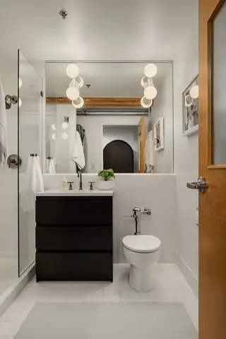 Capitol Hill Loft: A modern bathroom features a dark vanity cabinet, white tiled walls, and a large mirror reflecting double globe light fixtures