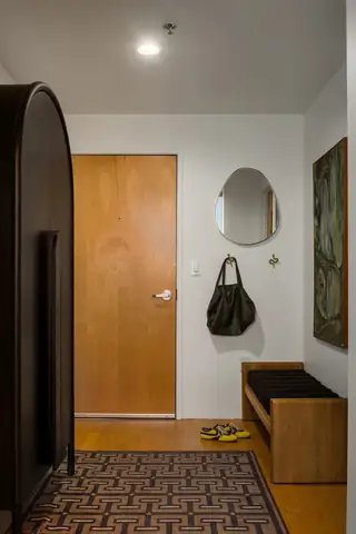 Capitol Hill Loft: A modern entryway features a light wood door, an organic-shaped wall mirror above a wooden bench, and a geometric pattern rug