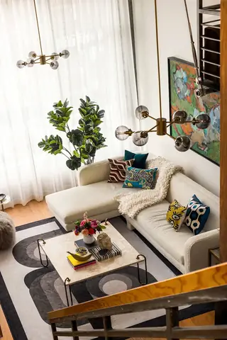 Capitol Hill Loft: A high-angle view of an eclectic living room featuring a cream bouclé sectional sofa, a marble coffee table, a geometric rug, and a modern brass chandelier