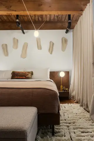 Capitol Hill Loft: A cozy modern bedroom features a wooden beam ceiling, cream drapery, a bed dressed in brown textured linens, and organic ceramic wall art