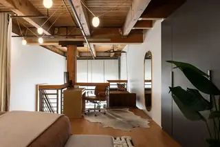Capitol Hill Loft: An industrial loft space features exposed wooden ceiling beams, a dedicated home office area with a brown leather chair and cowhide rug, and sleek dark wardrobes