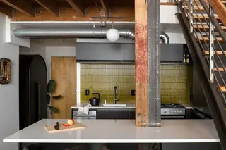 Capitol Hill Loft: Modern industrial kitchen featuring an olive green vertical tile backsplash, dark grey cabinets, a white island, and exposed timber and steel structural elements