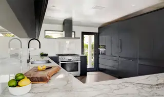 A modern minimalist kitchen features white marble countertops, sleek black cabinetry, and a stainless steel range stove.