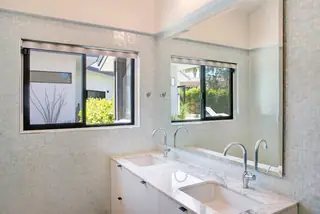 A modern bathroom features a double sink marble vanity with sleek chrome faucets against a wall of light blue iridescent mosaic tile.