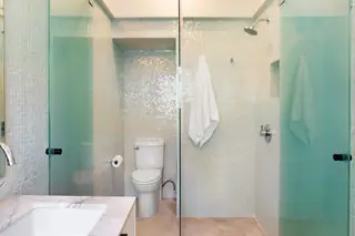 A modern bathroom featuring iridescent seafoam green mosaic tiles, a glass shower enclosure, and white porcelain fixtures.
