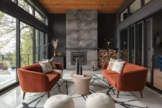 Chuckanut New Build, Bellingham: A moody modern living room features two rust-orange velvet sofas facing a tall concrete fireplace with stacked firewood