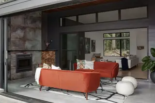 Chuckanut New Build, Bellingham: A modern covered patio living space features twin rust-orange velvet sofas, a black and white patterned rug, and a sleek dark fireplace
