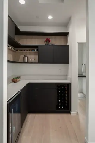 Chuckanut New Build, Bellingham: A modern home bar nook features dark charcoal cabinetry, built-in wine rack storage, light wood panel accents, and white quartz countertops