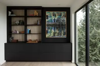 Chuckanut New Build, Bellingham: A modern home office features built-in matte black cabinetry, light wood-backed open shelving, and framed artwork beside floor-to-ceiling windows