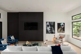 Chuckanut New Build, Bellingham: A modern living room features a dark slatted accent wall with a mounted television, a white sectional sofa, blue armchairs