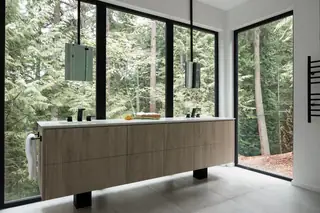 Chuckanut New Build, Bellingham: A modern bathroom features a floating light-wood double vanity set against expansive floor-to-ceiling windows overlooking a dense forest