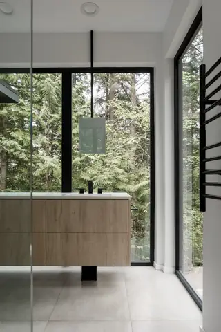 Chuckanut New Build, Bellingham: A modern bathroom features a floating light wood vanity cabinet and ceiling-suspended mirror positioned in front of floor-to-ceiling windows