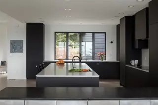 Chuckanut New Build, Bellingham: A minimalist modern kitchen features sleek dark cabinetry, a large central island with a light countertop