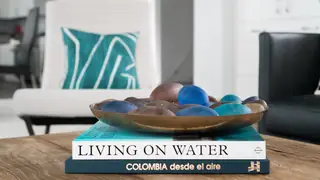 Stacked coffee table books topped with a shallow brass bowl and glass stones