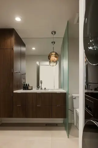 Edmonds Beach House: A modern bathroom features dark walnut cabinetry, a floating vanity with a white countertop, and an amber glass pendant light reflected in a large mirror