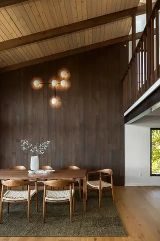 Edmonds Beach House: A mid-century modern dining space features a dark wood panel accent wall with a geometric globe sconce above a wooden table and woven-seat chairs