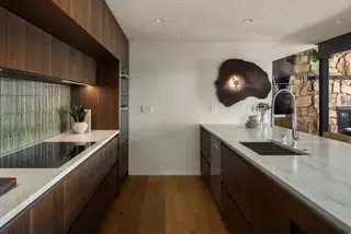 Edmonds Beach House: A modern kitchen featuring rich dark walnut cabinetry, light quartzite countertops, and a unique organic wood wall sconce