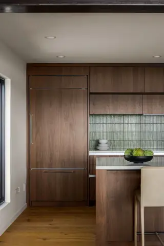 Edmonds Beach House: A modern kitchen features dark walnut cabinetry with a panel-ready refrigerator, a reeded glass tile backsplash, and a matching wood island