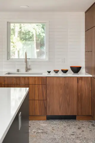 Greenwood Kitchen Design: A modern kitchen features warm walnut cabinetry paired with a white textured tile backsplash, quartz countertops, and terrazzo floor tile