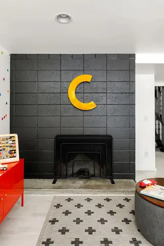 Issaquah Interior Design: A modern playroom features a painted black cinder block fireplace wall with a large yellow letter C above a black hearth screen