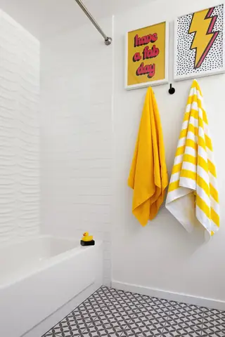 Issaquah Interior Design: A playful modern bathroom features a white bathtub, pop art wall prints, and hanging yellow towels above patterned floor tiles