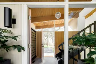 Issaquah Interior Design: A mid-century modern entryway seen through a framed doorway, featuring exposed wood beam ceilings, a hanging glass globe light
