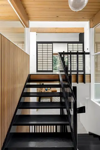Issaquah Interior Design: A view looking up a black open-riser staircase toward an upper landing featuring Japanese shoji sliding doors and a light wood-slatted ceiling