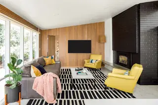 Issaquah Interior Design: A mid-century modern living room features vertical wood slat wall paneling, a dark grey leather sofa, twin yellow armchairs