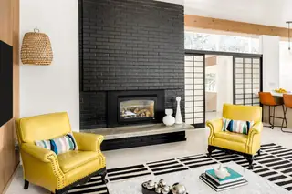 Issaquah Interior Design: A mid-century modern living room features a striking black brick fireplace flanked by two bright yellow leather armchairs on a black-and-white striped rug