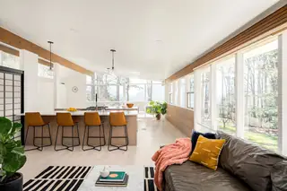 Issaquah Interior Design: A bright, open-plan mid-century modern living room and kitchen featuring large windows, a light wood island with cognac leather barstools