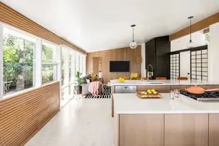 Issaquah Interior Design: An open-plan mid-century modern kitchen and living room featuring slatted wood wall paneling, light wood cabinetry, and large windows