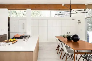 Issaquah Interior Design: A mid-century modern open kitchen and dining space features white seamless cabinetry, an exposed wood beam, a wooden dining table with white chairs