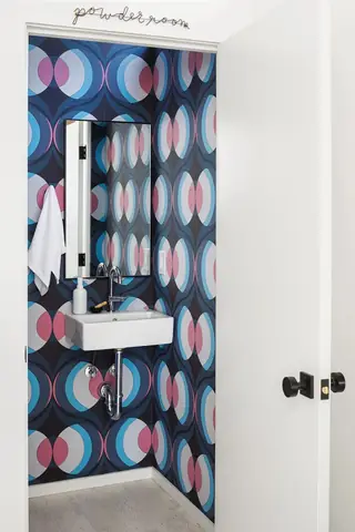 Issaquah Interior Design: A compact powder room viewed through an open white door features bold retro geometric wallpaper, a wall-mounted sink, and modern black accents