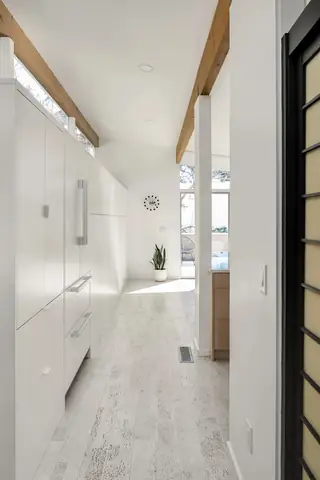 Issaquah Interior Design: A bright minimalist hallway lined with sleek white integrated kitchen cabinets, exposed wooden ceiling beams, and a potted plant at the far end