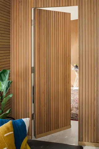 Issaquah Interior Design: A warm wood slatted door stands partially open within matching vertical wall paneling, offering a view into an adjacent room with a patterned rug