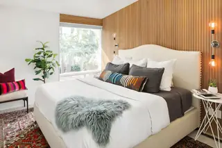 Issaquah Interior Design: A warm mid-century modern bedroom features a vertical wood slat accent wall behind an upholstered platform bed dressed in crisp white linens