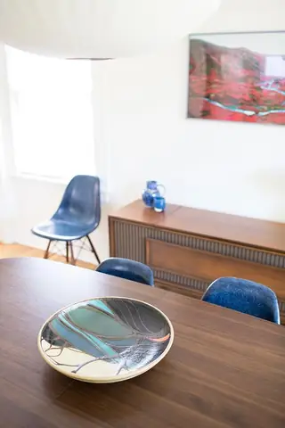 Madison Valley Design: A mid-century modern dining room features a decorative ceramic bowl on a dark wood table with blue chairs and a wooden credenza in the background