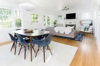 Madison Valley Design: A bright mid-century modern open-concept space features a dark wood dining table surrounded by navy blue shell chairs alongside a cozy living area